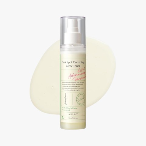 Axis-Y Dark Spot Correcting Glow Toner in a white pump bottle with label visible, set against a pale smear of product in the background for focus on the cosmetic.