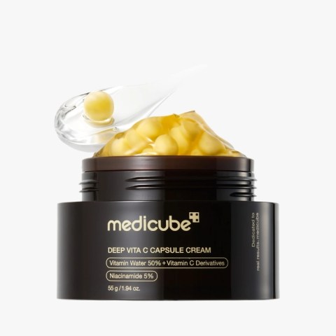 Medicube Deep Vita C Capsule Cream jar with a clear scoop releasing capsules into the open lid, on a white background, black container.