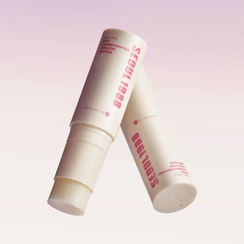Two white lip balm tubes with pink text leaning together on a soft pink gradient background.
