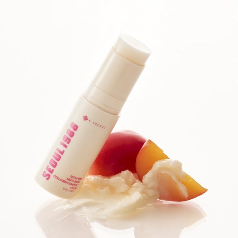 White pump bottle of skincare product beside peach slices and a dollop of cream on a reflective surface.
