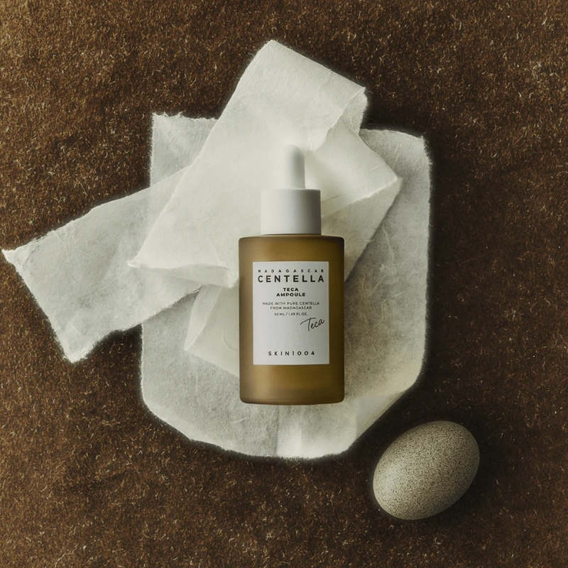 Brown glass dropper bottle of Centella serum on white tissue, against a brown textured surface.