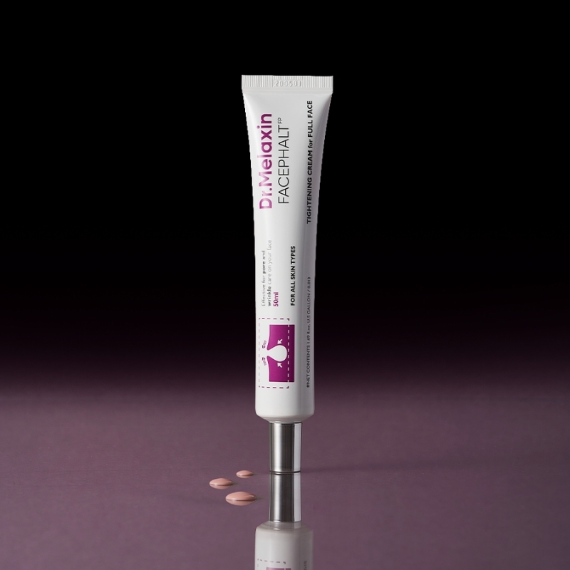White tube of Dr. Melaxin facial cream standing upright on a reflective dark purple surface with a few pink tablets nearby.