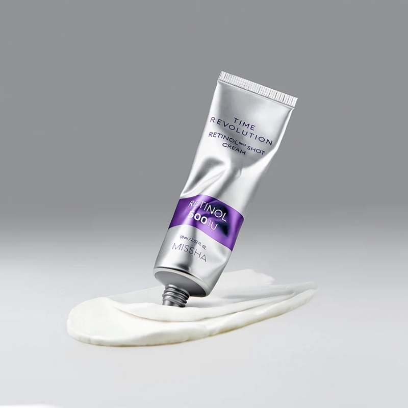 Missha Time Revolution Retinol 500 IU cream tube angled over a dollop of white cream against a gray background.