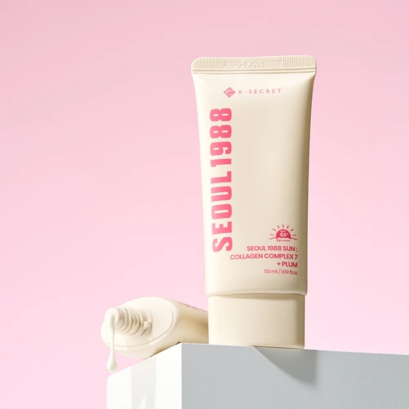 Cream cosmetic tube labeled 'SEOUL 1988' on a pastel pink background.