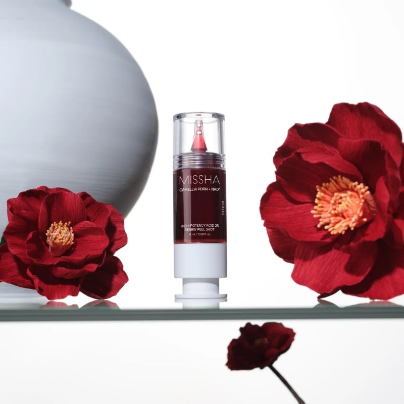 MISSHA high-potency acid 25 renewal peel shot bottle centered between red camellia flowers on a glass shelf.