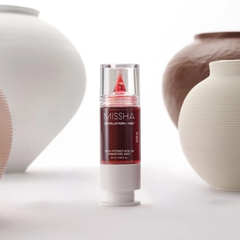 Missha skincare serum bottle with red liquid standing between ceramic vases on a white surface.